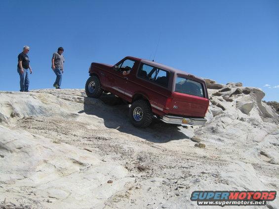 Red SUV climbing rocky terrain, two men watch from above