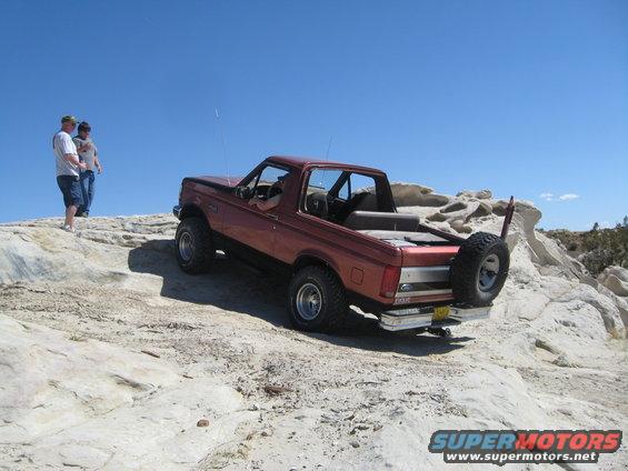Red Ford Bronco climbing rocky terrain with two people watching
