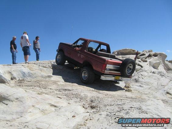 Red Ford Bronco climbing a rocky hill, with three people watching