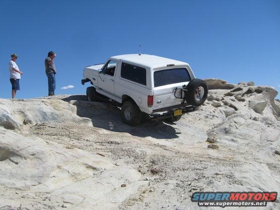 White SUV on a rocky incline with two people watching