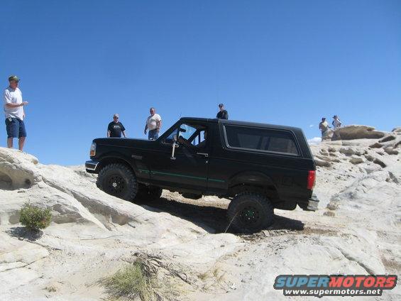 Black Ford Bronco climbing rocky terrain under a clear blue sky