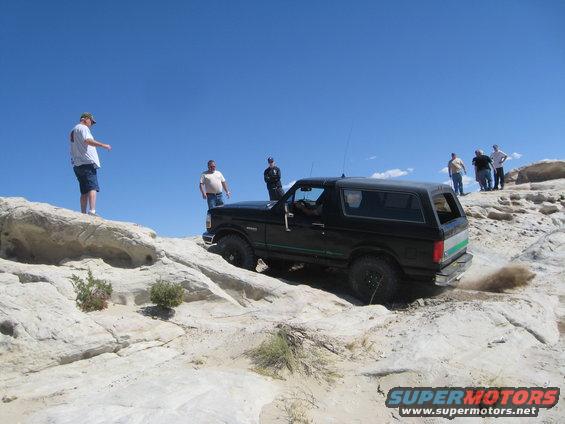 Black 1993 Ford Bronco climbing rocky terrain with people watching
