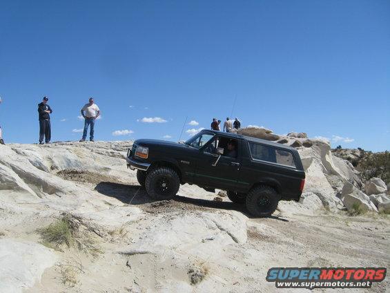 Black 1992 Ford Bronco climbing a rocky incline under a clear blue sky