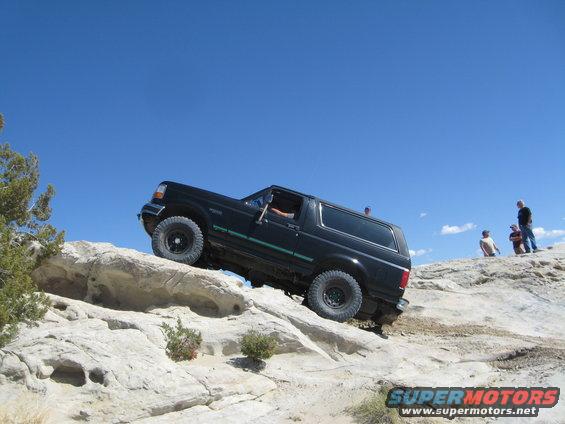 Black 1993 Ford Bronco climbing a rocky incline under a clear blue sky