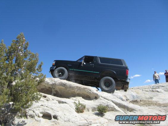 Black Ford Bronco climbing over rocks on a trail with two people watching