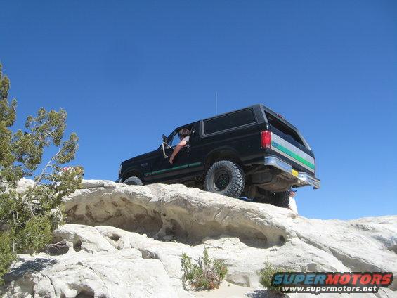 Black Ford Bronco climbing a rocky incline under a clear blue sky