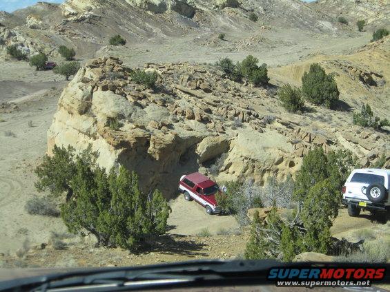 1993 Ford Bronco and white SUV driving on dirt path in desert canyon