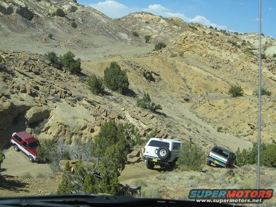 Three SUVs driving on a dirt path in a rocky, desert-like landscape