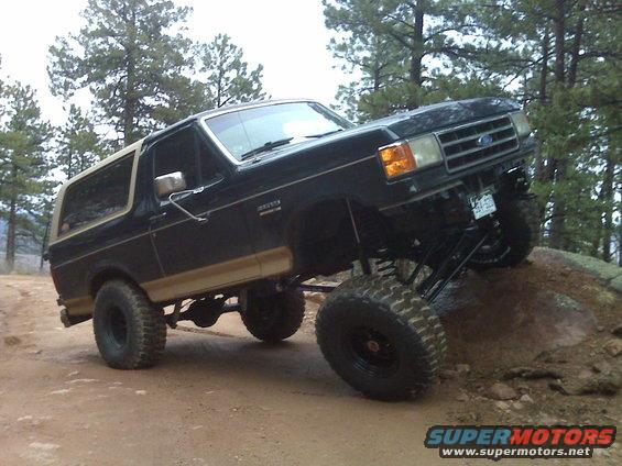 Black Ford Bronco with tan trim, lifted suspension, large tires, driving over rocks on a dirt trail