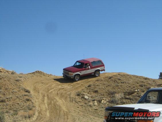 red and white SUV climbing a dirt hill, another white vehicle in foreground