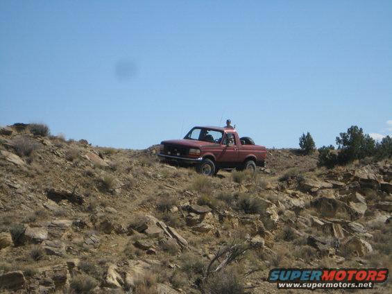 red pickup truck driving up a rocky, barren hill under a clear blue sky