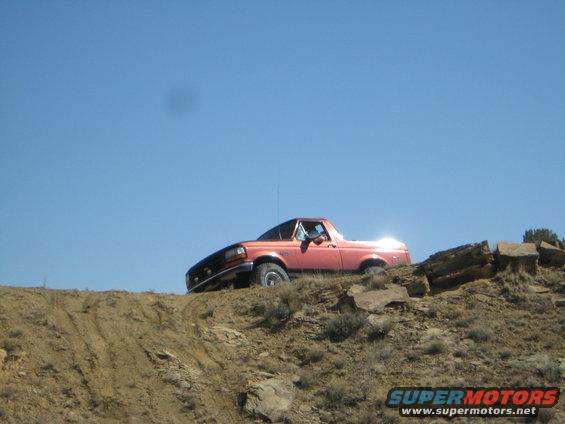 Orange 1993 Ford Bronco driving off-road on a dirt hill