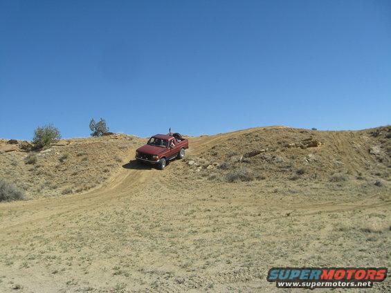 Red pickup truck driving up a dirt hill on a sunny day
