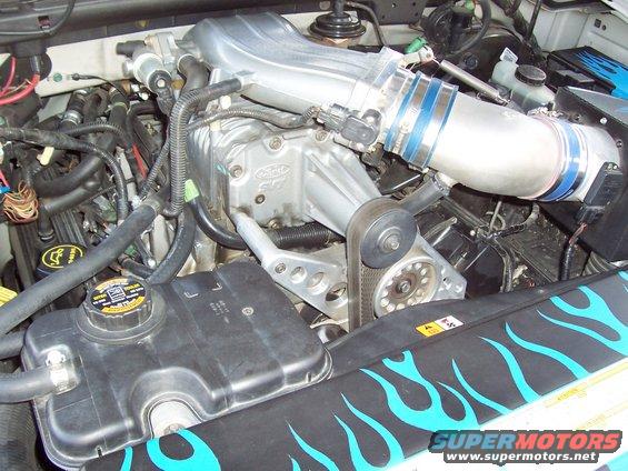 Close-up of a Ford engine with a supercharger and blue flame decals on a radiator cover