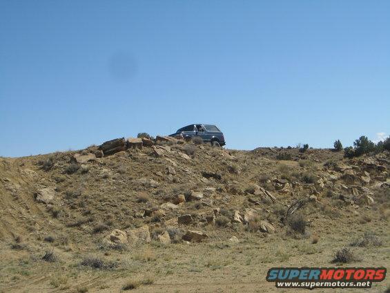Dark SUV on rocky hill, front quarter view. Some dirt and brush visible