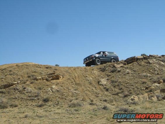 Dark SUV climbing a rocky, dirt hill under a clear blue sky