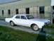 1966 Oldsmobile Cutlass - A white 1966 Oldsmobile Cutlass sedan is parked in front of a building.