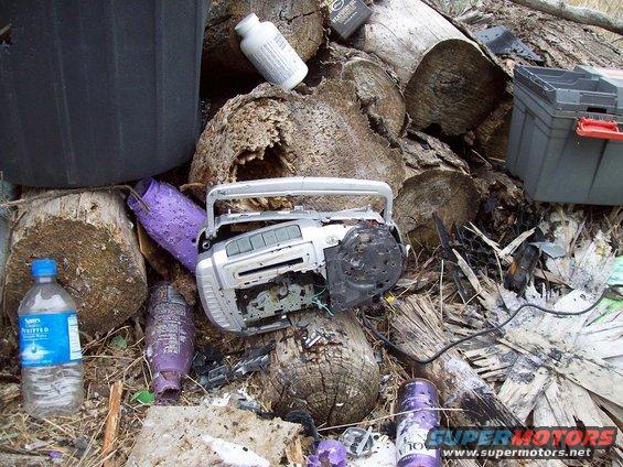 Broken silver boombox, purple bottles, and a water bottle among logs and debris