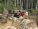 1979 Ford Bronco - Off-road vehicles tackle a challenging, boulder-strewn path in a wooded area.