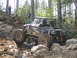 1979 Ford Bronco - A heavily modified off-road buggy tackles a challenging rocky terrain in a wooded area.
