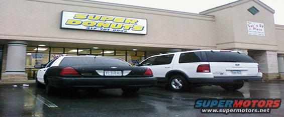 Black and white police car and white SUV parked in front of Super Donuts