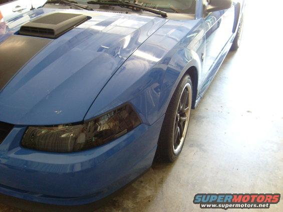 Front corner of a blue Ford Mustang with a black hood stripe and a hood scoop