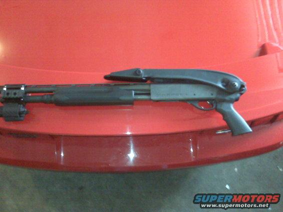 Black shotgun with a tactical light mounted on the barrel, resting on a red surface