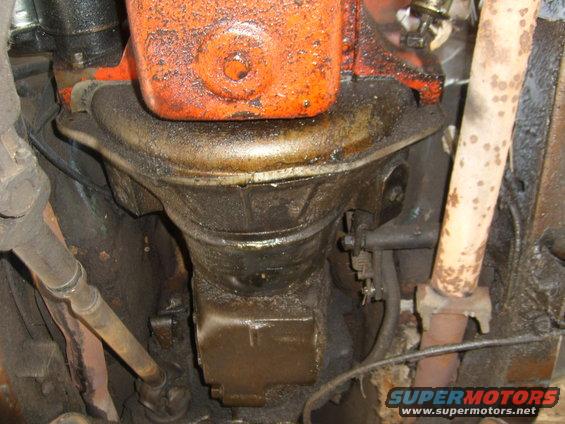 Underside view of an engine with an oil pan and a rusty exhaust pipe. Lots of grease and grime visible