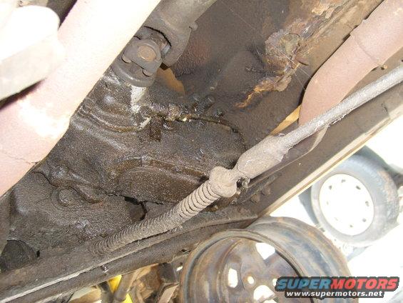 Underside view of vehicle drivetrain with rust and a visible tire