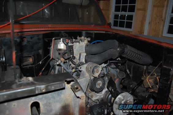Orange vehicle engine bay with visible engine components, hoses, and wiring. Watermark reads SUPERMOTORS.NET