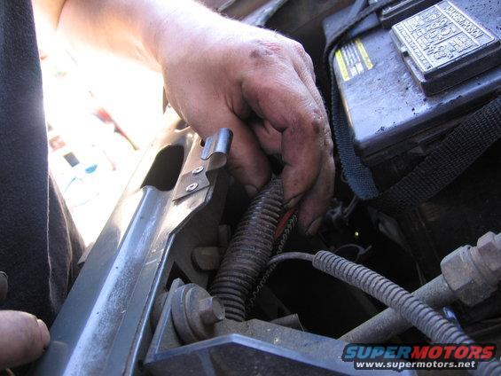 1987 Ford Bronco engine compartment with a hand manipulating wiring near the battery
