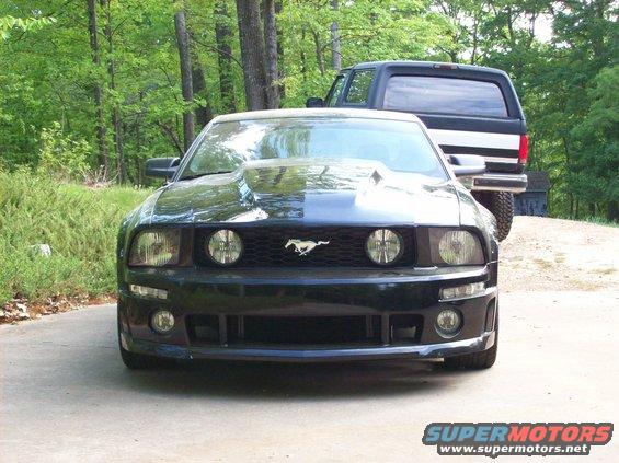 Black Ford Mustang with a scoop on the hood, parked in front of a black SUV
