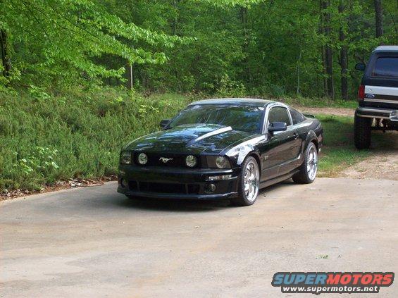 Black Ford Mustang with aftermarket hood scoop parked on a concrete driveway