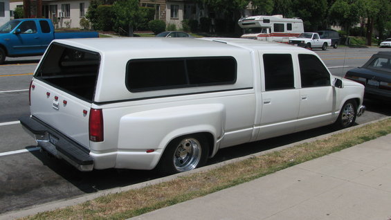 white extended cab dually pickup truck with a camper shell parked on street