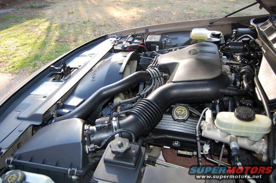 Engine bay with air intake, fan, battery, and fluid reservoirs visible. Oil cap has an oil can symbol