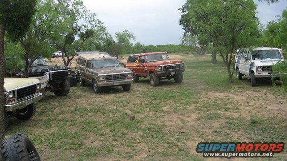 Red 1978 Ford Bronco with a camper shell, parked on a dirt lot with trees