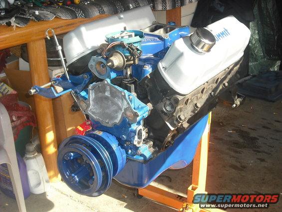 Blue V8 engine on an orange stand. White valve covers have 'SUMMIT' written on one