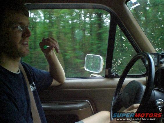 Interior view of a vehicle with a man driving, trees visible through the window