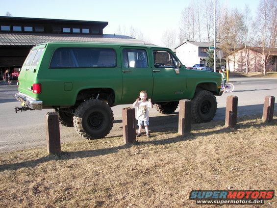 Green lifted SUV with large tires parked on grass, side view