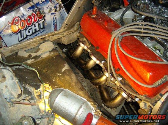 Engine bay with orange valve covers, exhaust headers, and Coors Light cans