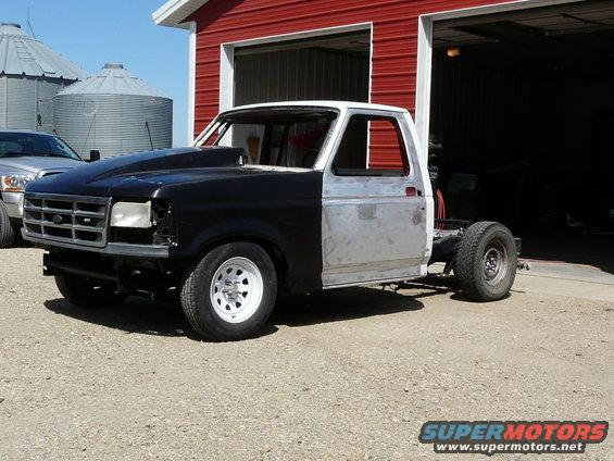 Ford F-Series truck body, black hood, bare metal cab, sitting outside red barn