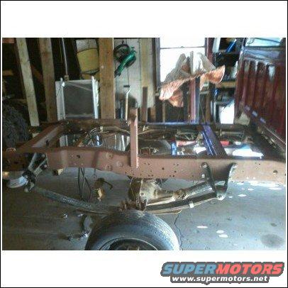Truck frame and suspension in a garage, with a red cab visible on the right