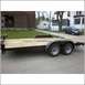2005 Ford F-250 - A flatbed trailer with a wooden deck and dual axles is parked on a street in front of a house.