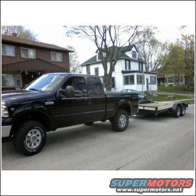 2005 Ford F-250 pickup truck, side view, towing a dual-axle flatbed trailer