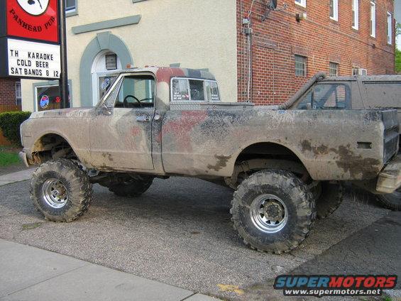 Mud-covered lifted pickup truck with large tires, parked next to another vehicle