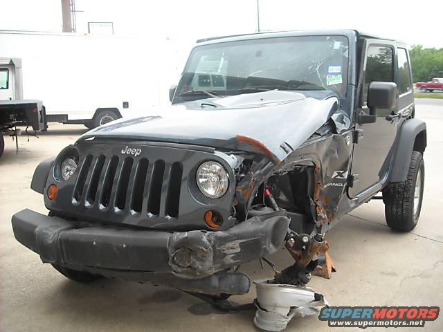 Wrecked dark gray Jeep Wrangler front view with extensive damage to the front passenger side