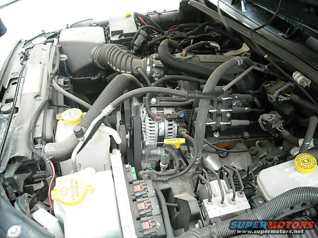 Engine bay of a modern vehicle, showing hoses, wires, alternator, and fuse box