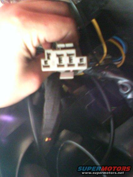 Hand holding a white electrical connector with yellow and blue wires attached