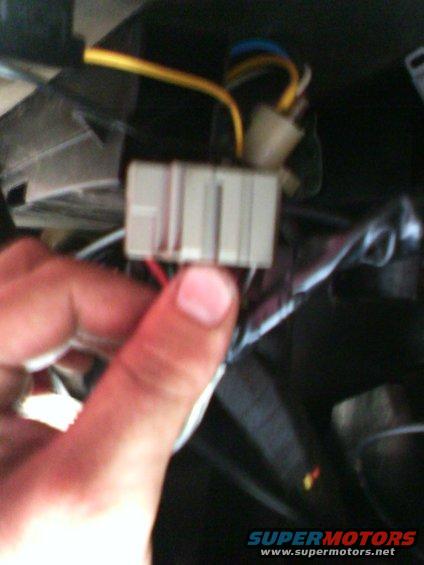 Close-up of a hand holding a wiring harness connector with yellow and blue wires