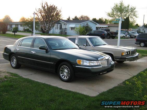 Dark green sedan parked in front of a tan sedan on a suburban driveway